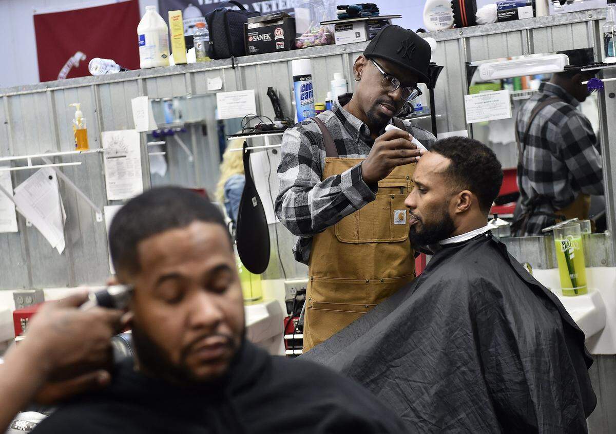 Lamonte McIntyre (standing) spent 23 years in the Kansas prison system for a crime he did not commit and struggled to get medical care for a foot problem. Now free, he recently graduated from barber school and plans to become an instructor. McIntyre gives a specialty cut to customer Rivero Echols of Kansas City, Kansas.