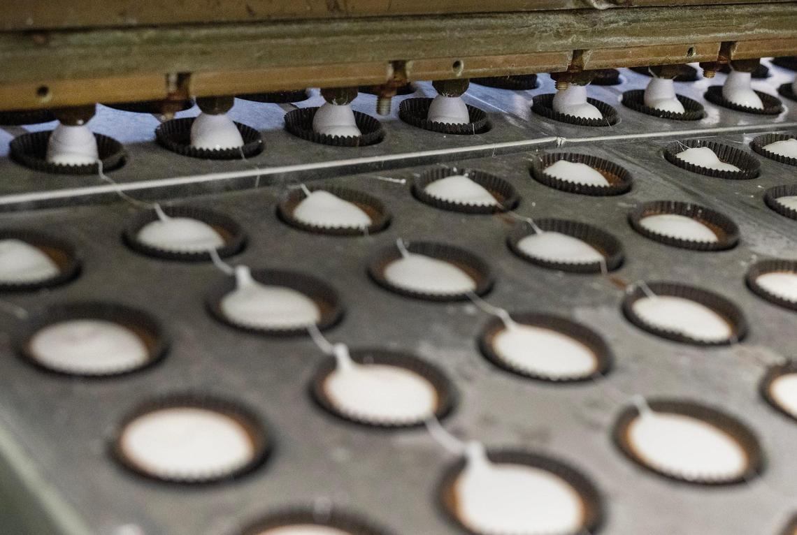A vintage 1950s-era machine squirts marshmallow cream into chocolate cups during a production run.