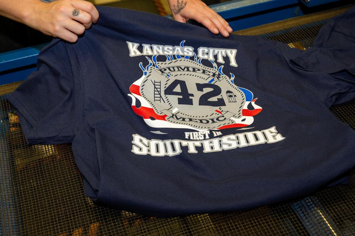 Memorial T-shirts honoring Kansas City Fire Department firefighter Graham Hoffman emerge from the dryer and are readied for distribution at E2 Embroidery & Screenprinting on Tuesday, May 13, 2025, in Kansas City. The shop has begun producing these shirts to honor Hoffman, who was fatally stabbed inside an ambulance.