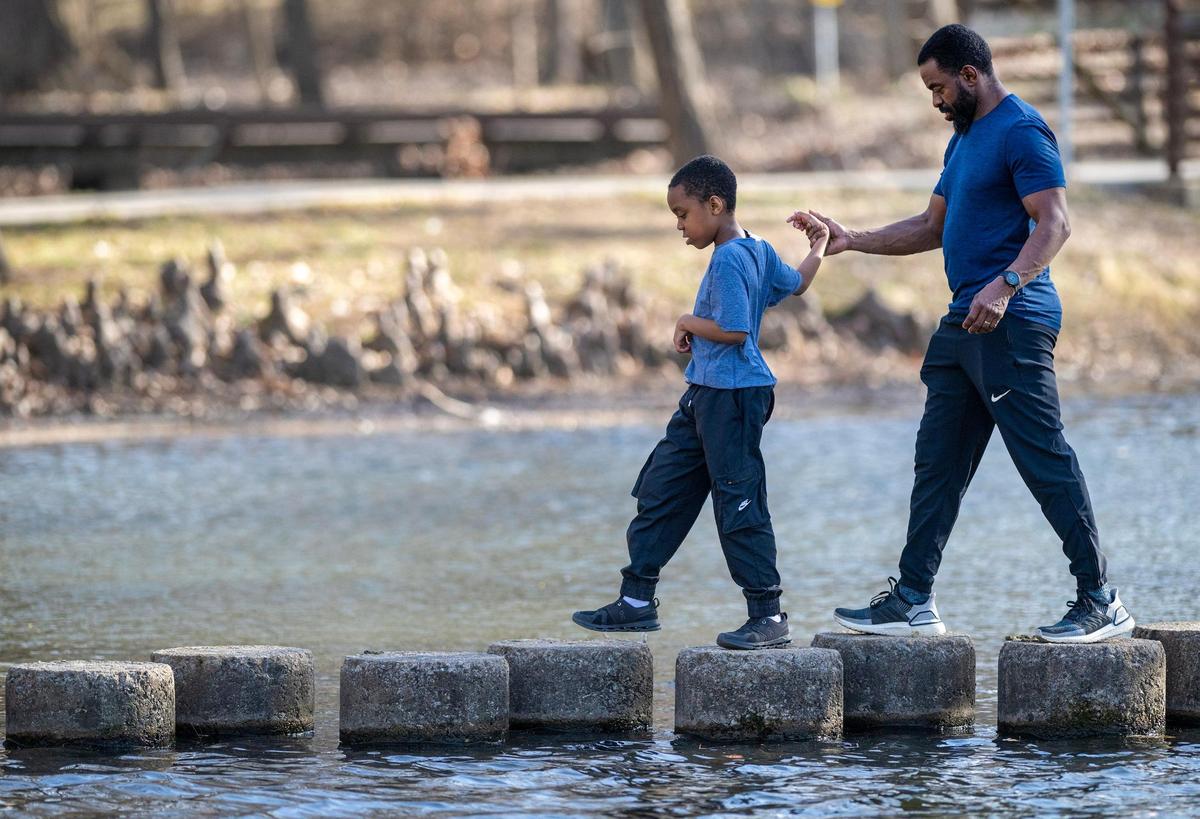 Ethan Musee, 9, held hands with his father, Samuel Musee as they carefully navigated the steps across the lake at Antioch Park while enjoying the unseasonably warm weather before a cold front moved in Tuesday in Merriam.. The pair were visiting the park with mom, wife, Belinda Musee. The family lives in Lenexa.