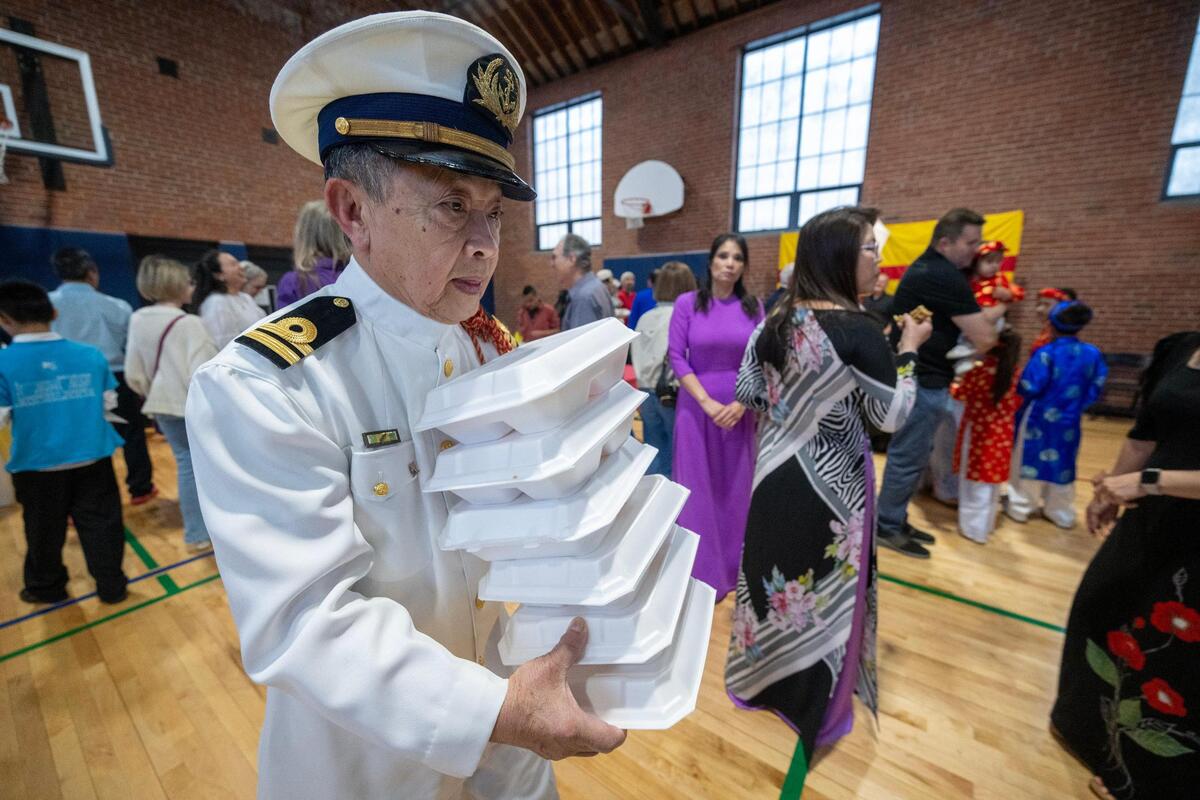 Ty Bui, 77, center, of Overland Park, a former Navy Captain for the South Vietnamese, carries meal boxes for family members during a reception.