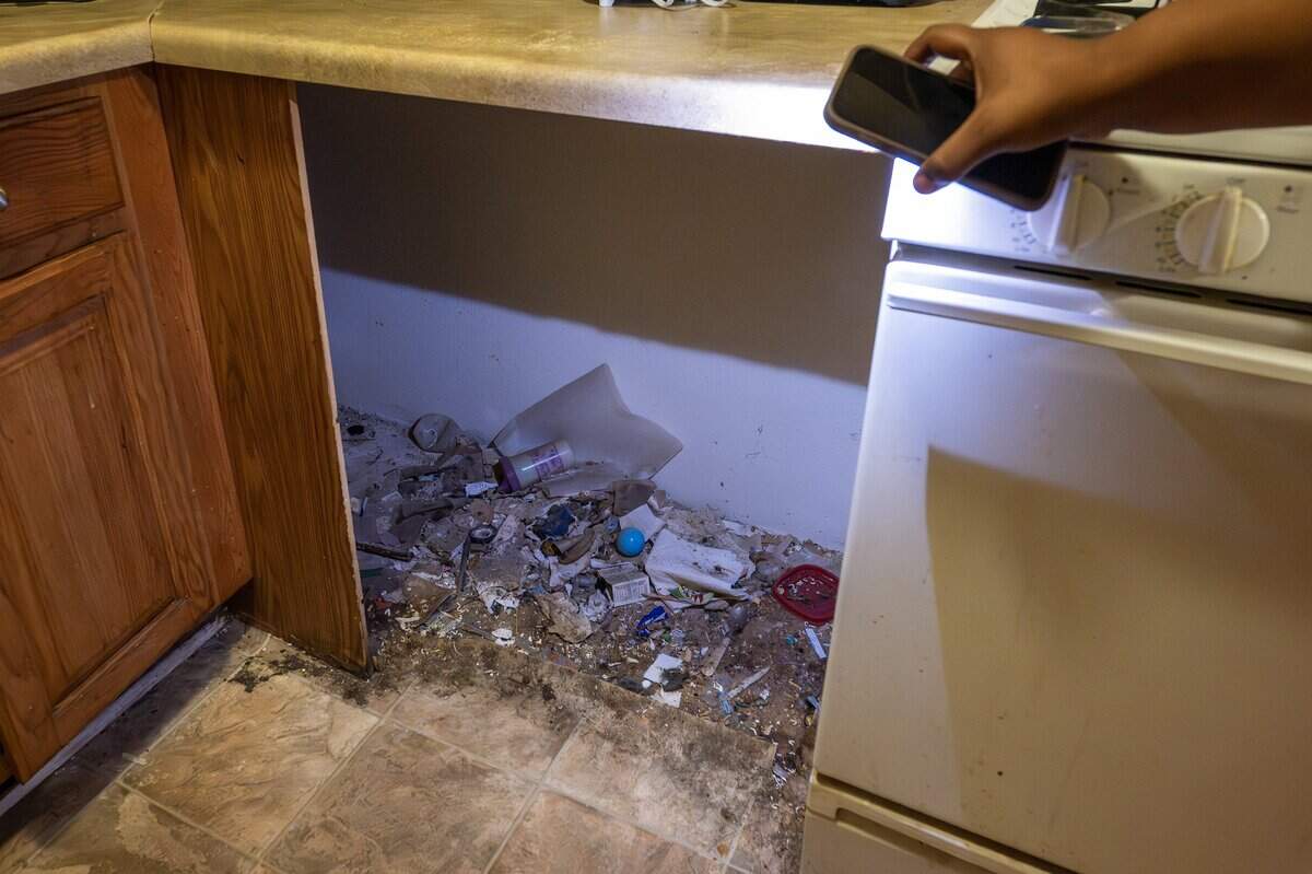 Mikayla Daniels uses her phone's flashlight to illuminate debris in the empty space where a dishwasher once sat in her kitchen at Sage Crossing Apartments on Wednesday, Sept. 17, 2025, in Lee's Summit.