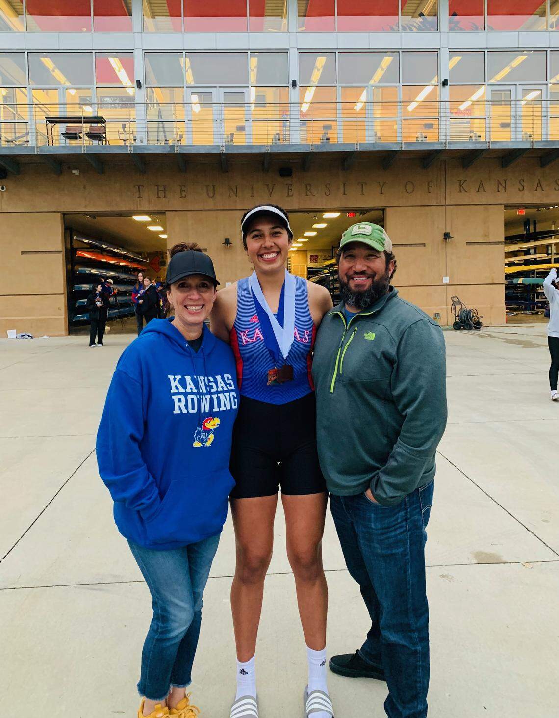 Isabela “Izzy” Estes smiles for a photo with her parents outside of the University of Kansas boathouse in Lawrence after her first novice race in October 2021.