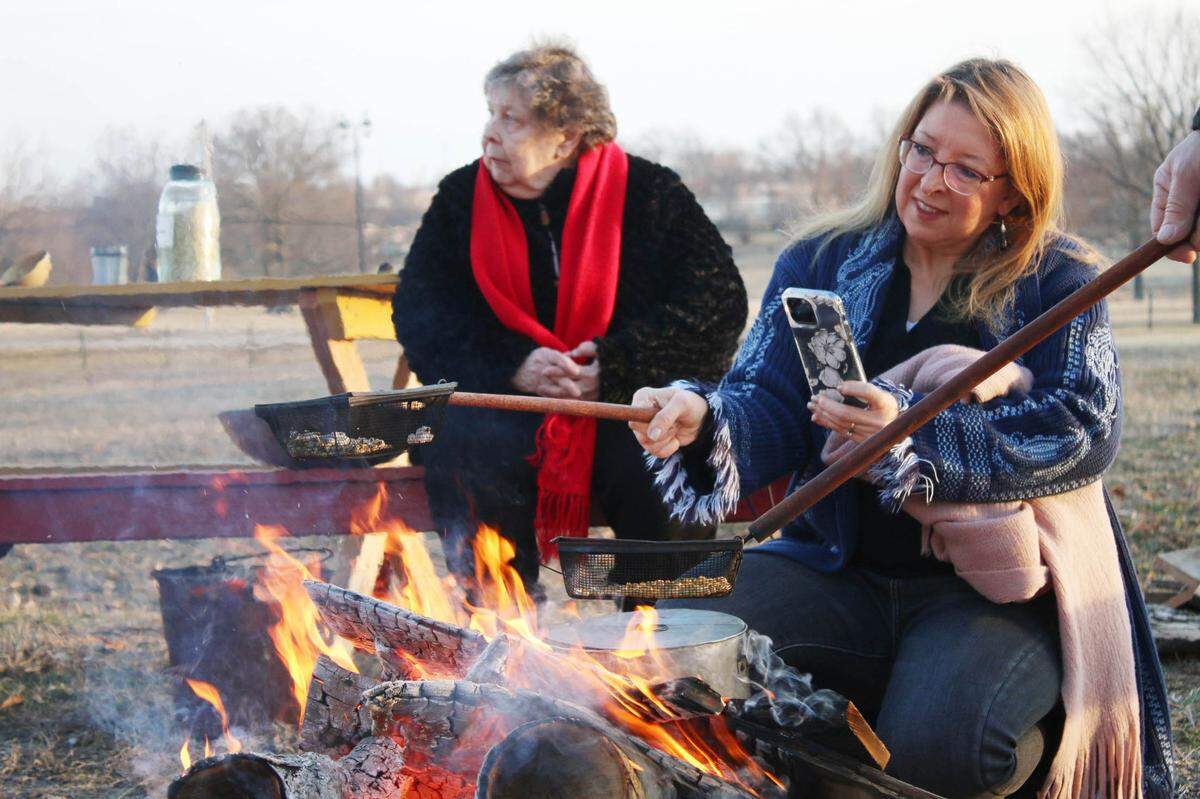 Olathe resident Jennifer Cisneros pops popcorn over a bonfire as her mother, Donna Obrist, warms up by the fire at the Mahaffie Stagecoach Stop and Farm Feb. 25.