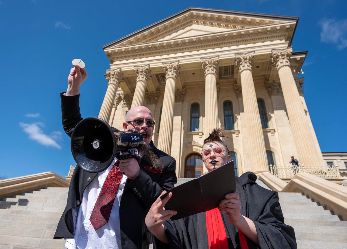 Satanic Grotto leader Michael Stewart recites a passage from a black book while holding a communion host, as Jaee Frazee holds the book open during a Black Mass ritual near the steps of the Kansas State Capitol on Friday, March 28, 2025, in Topeka.