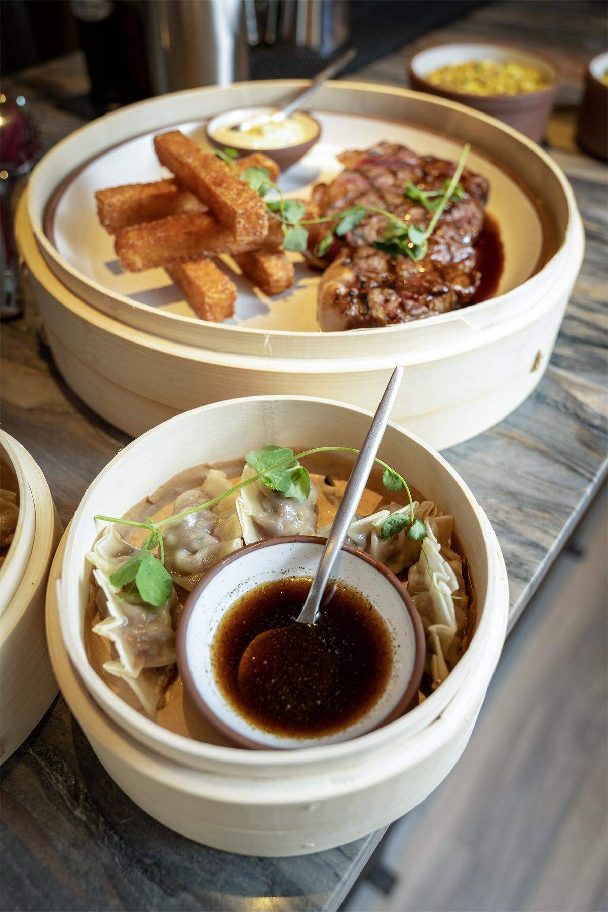 A5 Wagyu Dumplings with charred scallion dash, foreground, and Creekside Farms Steak Frites with potato roti and tarragon aioli at Palm Beach Club, a restaurant and bar opening this month at 14 E. 14th Street in Kansas City's Power and Light District.