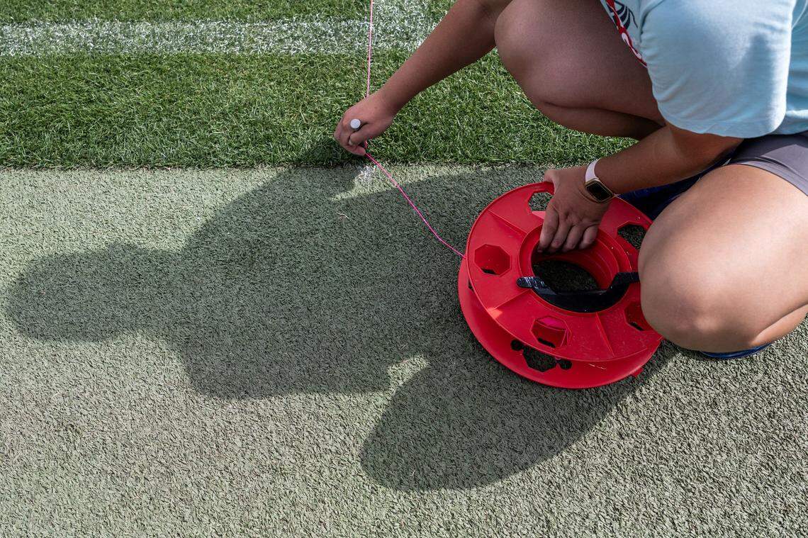 Julie Kessler, Kansas City Current grounds-crew member, stretches a string line to guide a line-marking machine applying green paint to cover existing pitch lines in preparation for rugby at CPKC Stadium on Tuesday, April 14, 2026, in Kansas City.