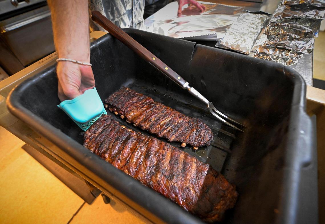Pitmaster Nathen Cameron pulls some ribs hot out of the smoker. Customers are served ribs wrapped in aluminum foil with white bread and a house-made barbecue sauce.