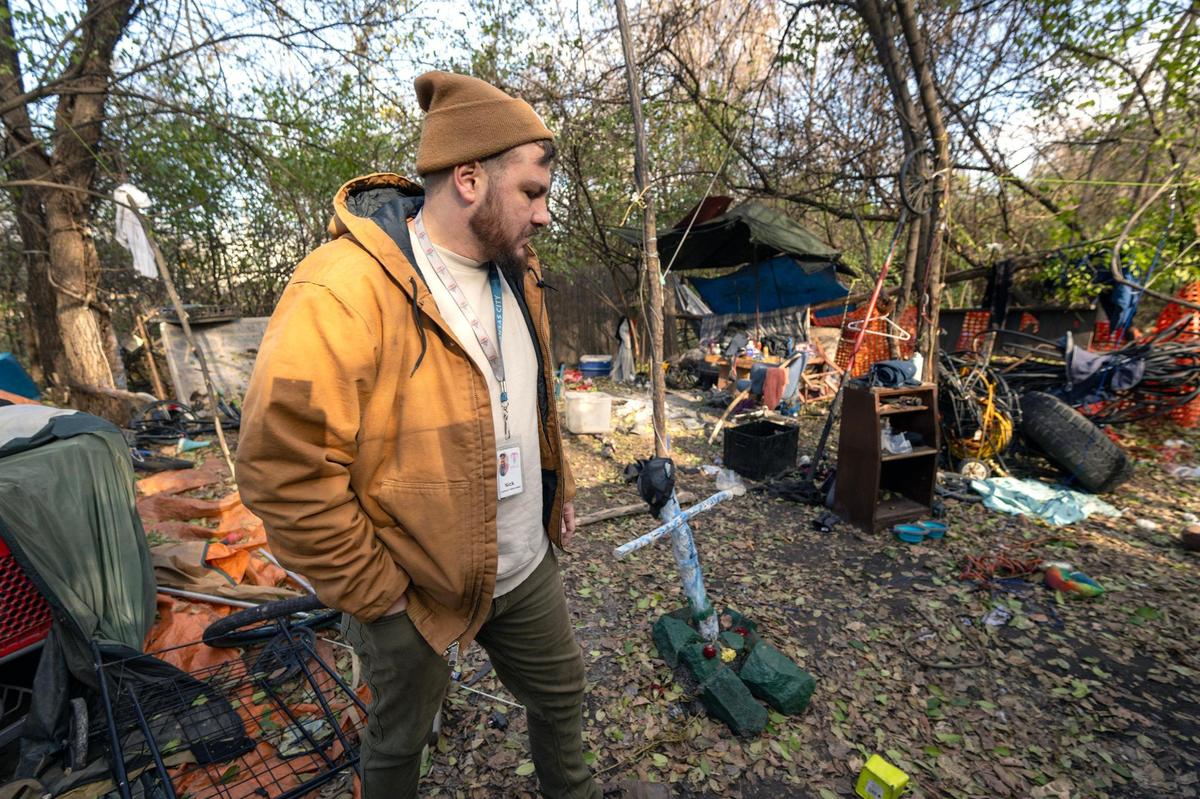 Nick Allen, the street outreach coordinator for the Office of Unhoused Solutions, walks through a homeless camp and past a cross memorializing two individuals killed in May, 2022.