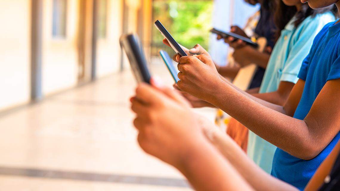 Close up shot, group of children hands busy using smartphone at school corridor - concept of social media, playing games, technology and education
