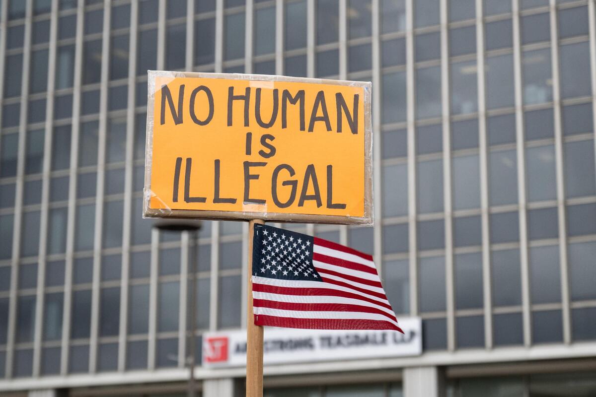 A sign held up in Washington Square Park with the building housing Kansas City’s federal immigration court in the background.