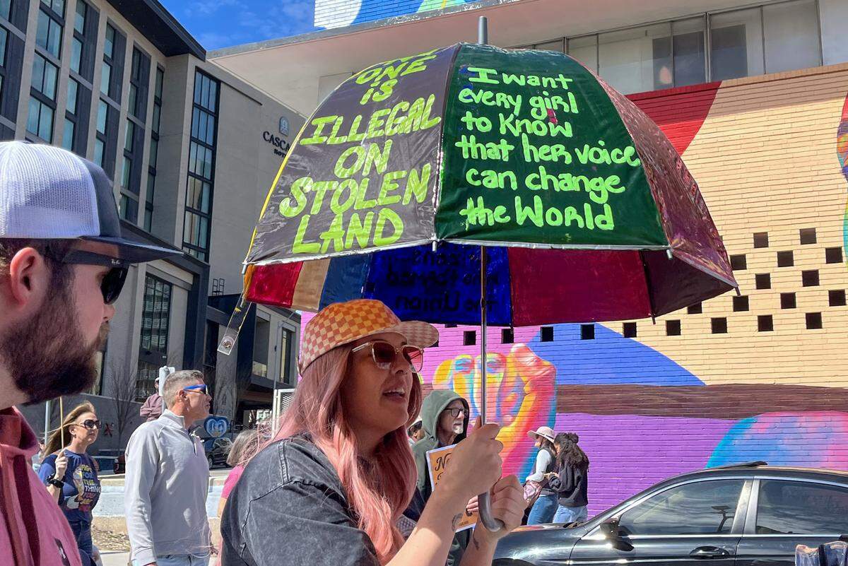 A woman holds up an umbrella painted with protest slogans along Broadway Boulevard in Kansas City during a No Kings protest against the Trump administration on Saturday, March 28, 2026.