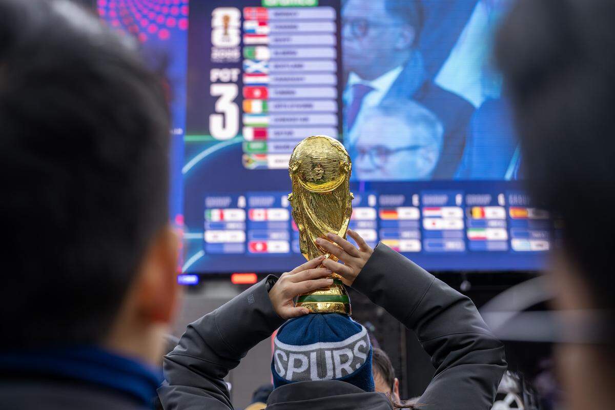 A fan holds a replica FIFA World Cup trophy as the group teams are announced during the World Cup draw watch party at the Power & Light District on Friday, Dec. 5, 2025, in Kansas City.