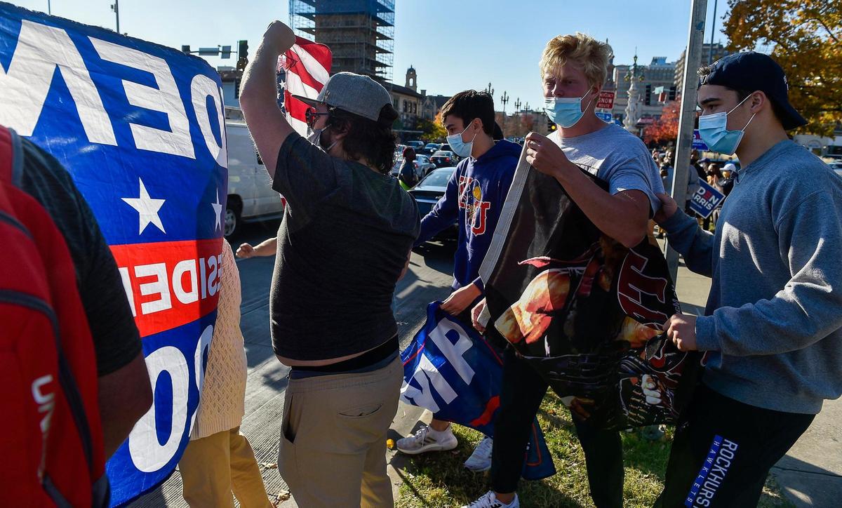 Biden supporters use an American flag to block the banner of Trump supporters who arrived as more than 100 Biden-Harris supporters turned out to Mill Creek Park Saturday afternoon.