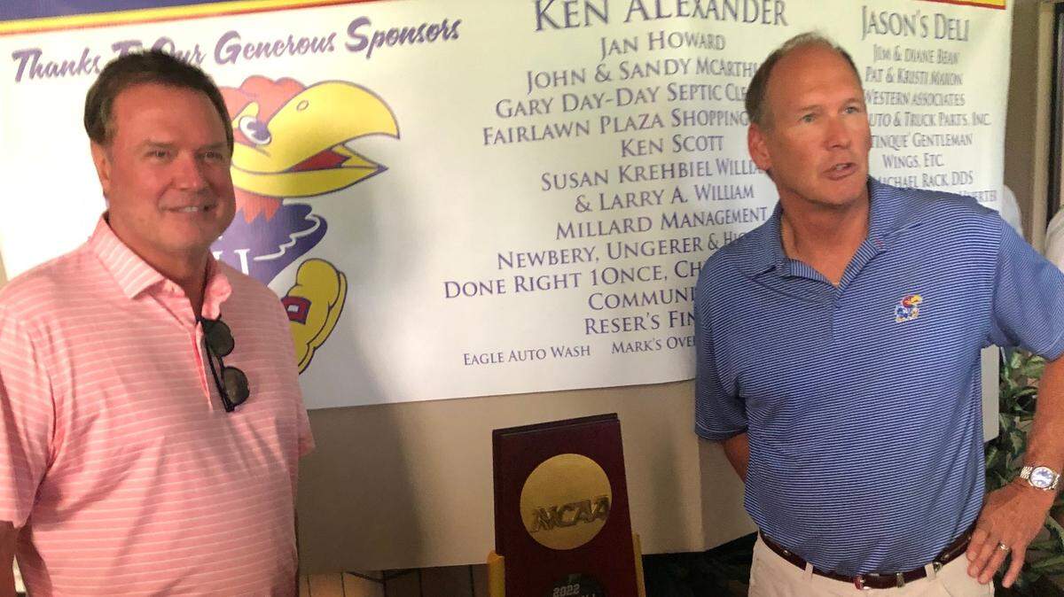 Kansas men’s basketball coach Bill Self, left, and football coach Lance Leipold pose next to the 2022 NCAA men’s basketball title trophy, won by KU.