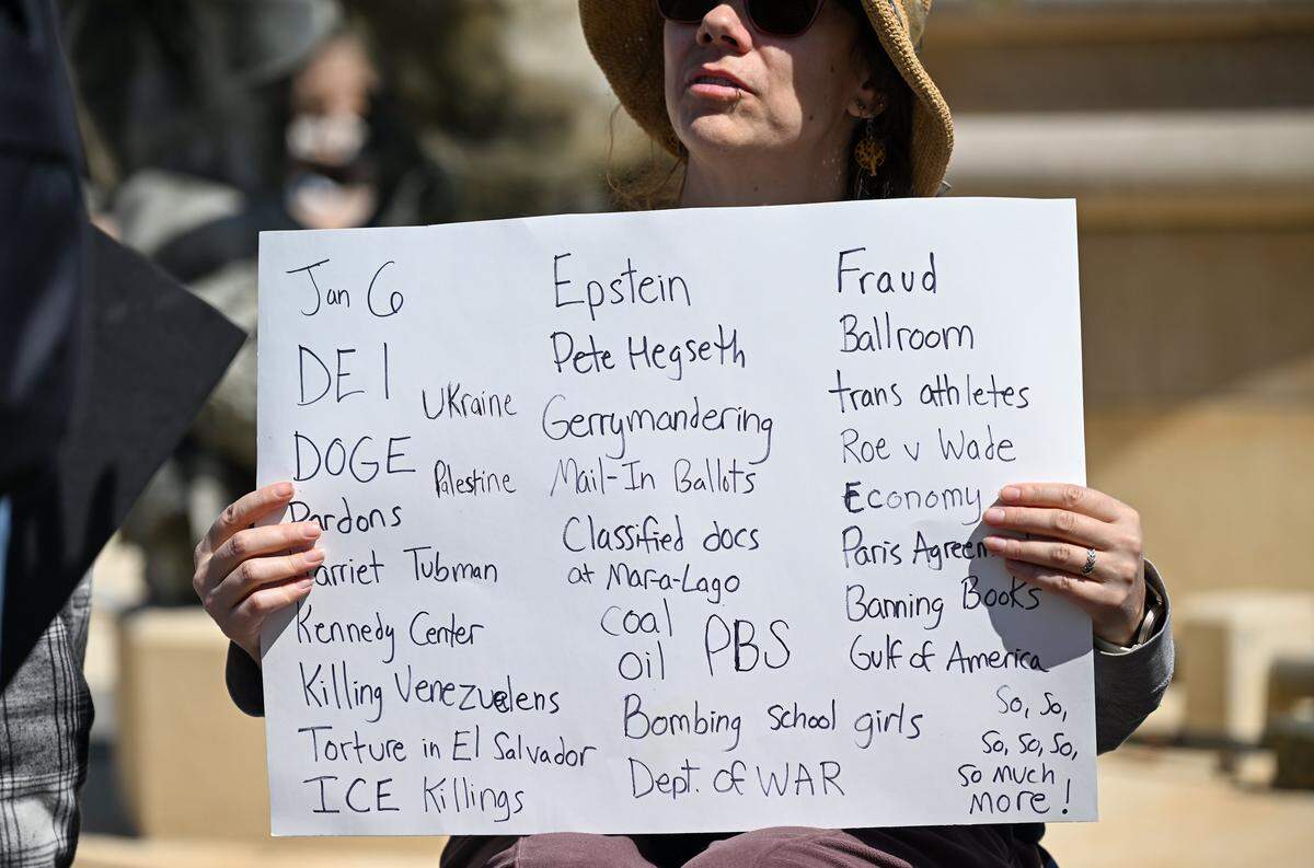 A protester holds up a sign at a No Kings rally against the Trump administration in Mill Creek Park near the Country Club Plaza on Saturday, March 28, 2026, in Kansas City.