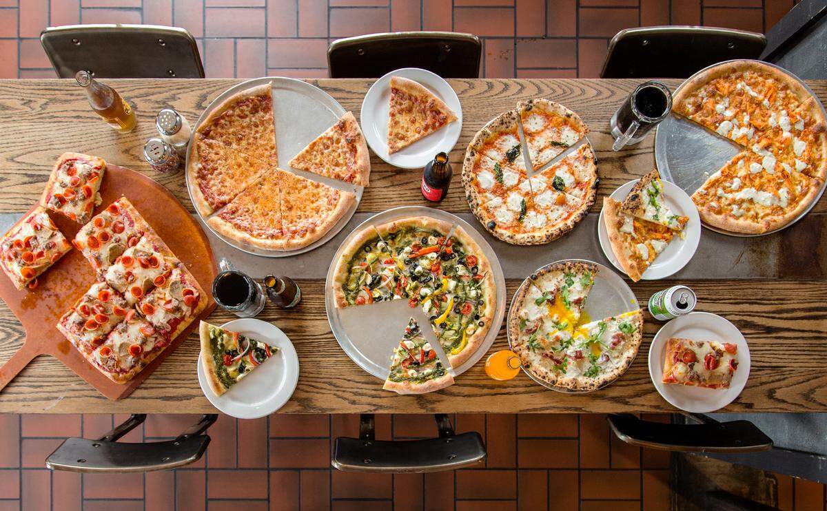 Various pizzas are arranged at a table inside Providence Pizza.