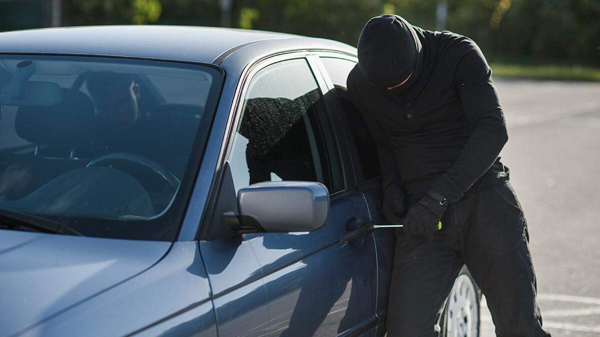 An offender in black clothes and mask is trying to steal a car in a parking lot