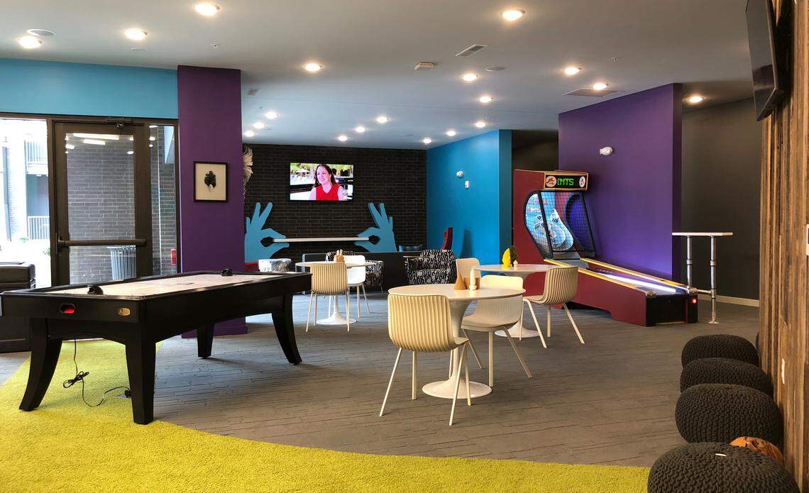 An arcade lounge at Crossroads Westside Apartments is decked out with TVs, Skee-Ball and air hockey. The windows look out to a saltwater pool with views of Union Station.