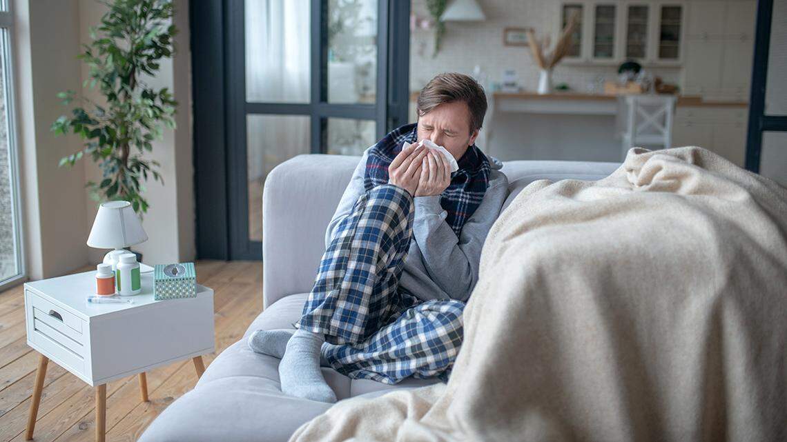 Sneeze and cough. Businessman sitting on sofa while being on sick leave and having sneeze and cough