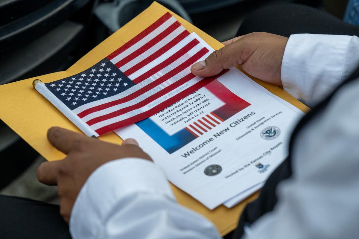 Jonathan Castro, 29, a native of Ecuador, holds a flag and his citizenship documents during the naturalization ceremony at Kauffman Stadium. Castro, who works in underground construction, lives with his family in Grandview,