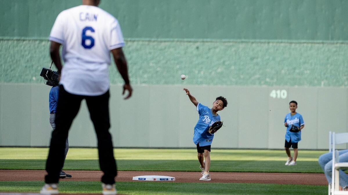 For the ceremonial first pitch, Cameron Cain, 8, completes a relay from center field and throws a ball to his dad and former Kansas City Royals center fielder Lorenzo Cain during a retirement ceremony at Kauffman Stadium on Saturday, May 6, 2023, in Kansas City. Cain signed a ceremonial one-day contract to retire as a Royal.