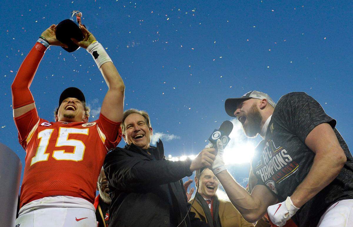 Kansas City Chiefs quarterback Patrick Mahomes lifts the Lamar Hunt trophy as CBS sportscaster Jim Nantz holds the microphone for Travis Kelce who sings “You’ve got to fight for your right to party!” onstage after the Chiefs defeated the Tennessee Titans 35-24 in the AFC championship game on January 19, 2020, at Arrowhead Stadium.