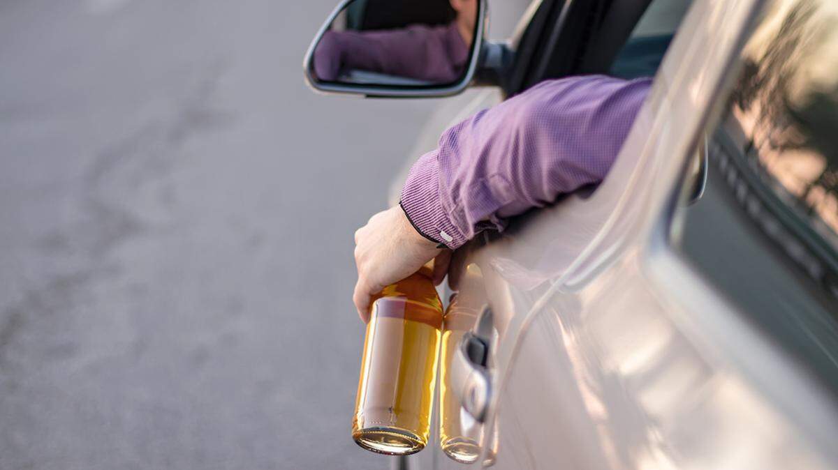 concept of alcohol, dangerous driving. drink and drive. man drinks off a bottle of beer while driving car. driver throws the bottle out of the car window. drunk driving. alcohol abuse alcoholism dui driving under the influence