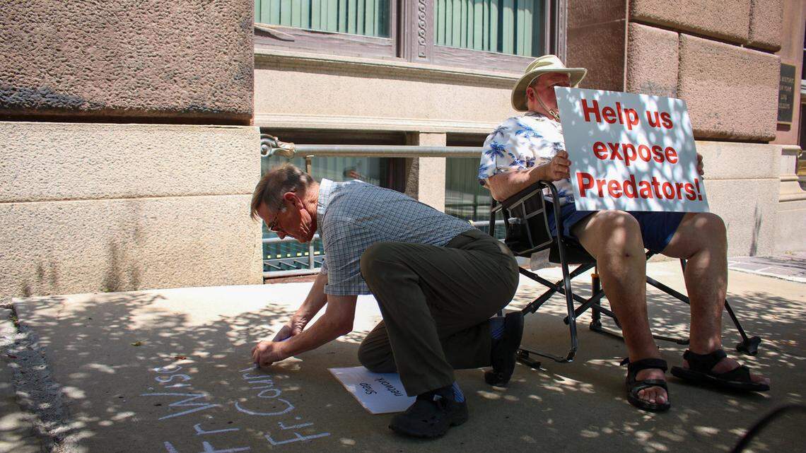 David Clohessy, director of Missouri Survivors Network of those Abused by Priests (SNAP) writes the names of priests publicly accused of abuse on the sidewalk in front of the Diocese of Kansas City-St. Joseph on Aug. 1, 2024. Tom White, a SNAP supporter sits beside Clohessy with a sign that reads “Help us expose predators.”