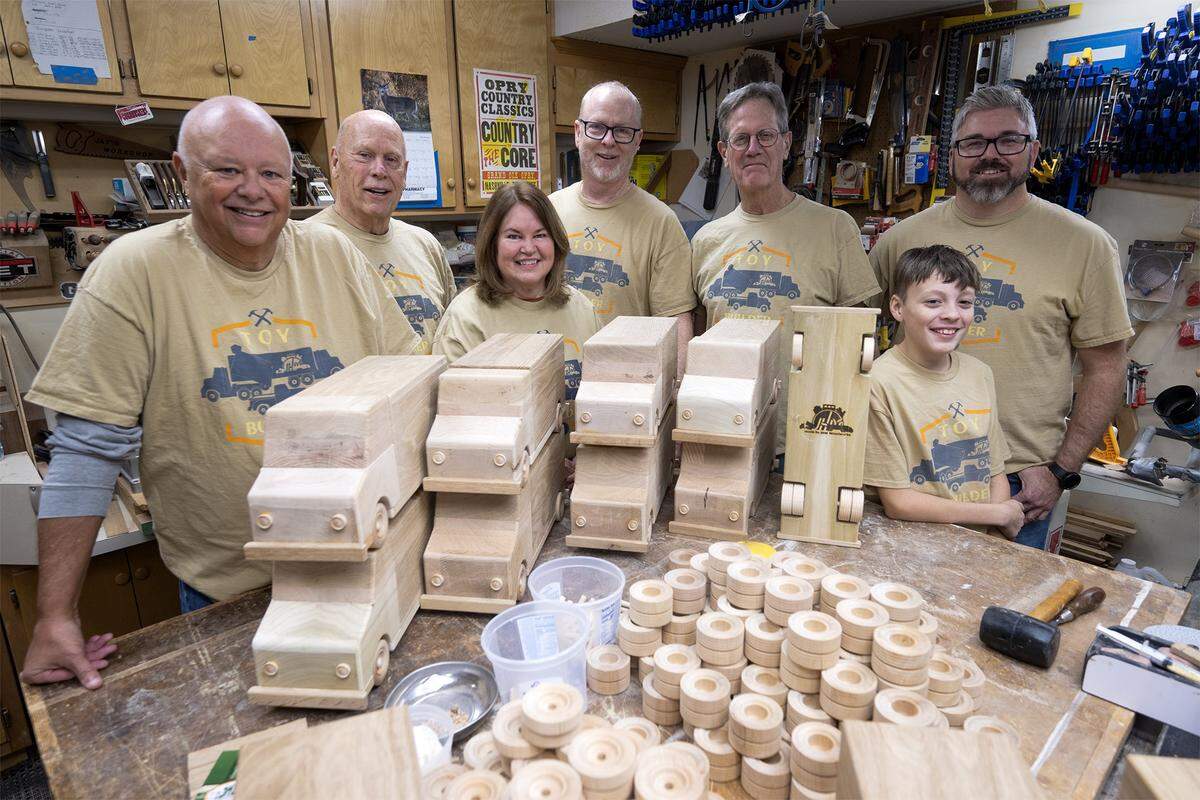 Jay Morris and his wife, Mary Ann Morris, center, stand with volunteers Tony Kisner, from left, Steve “Woody” Wood, Steve Dillon, and Brandon and Bryce Bradshaw after completing the assembly of toy trucks made from donated wood scraps on Tuesday, Dec. 2, 2025, in Lawrence, Kansas. Led by Jay Morris of JHM Woodworks, who will donate the 115 handcrafted trucks to the Toys for Tots program.