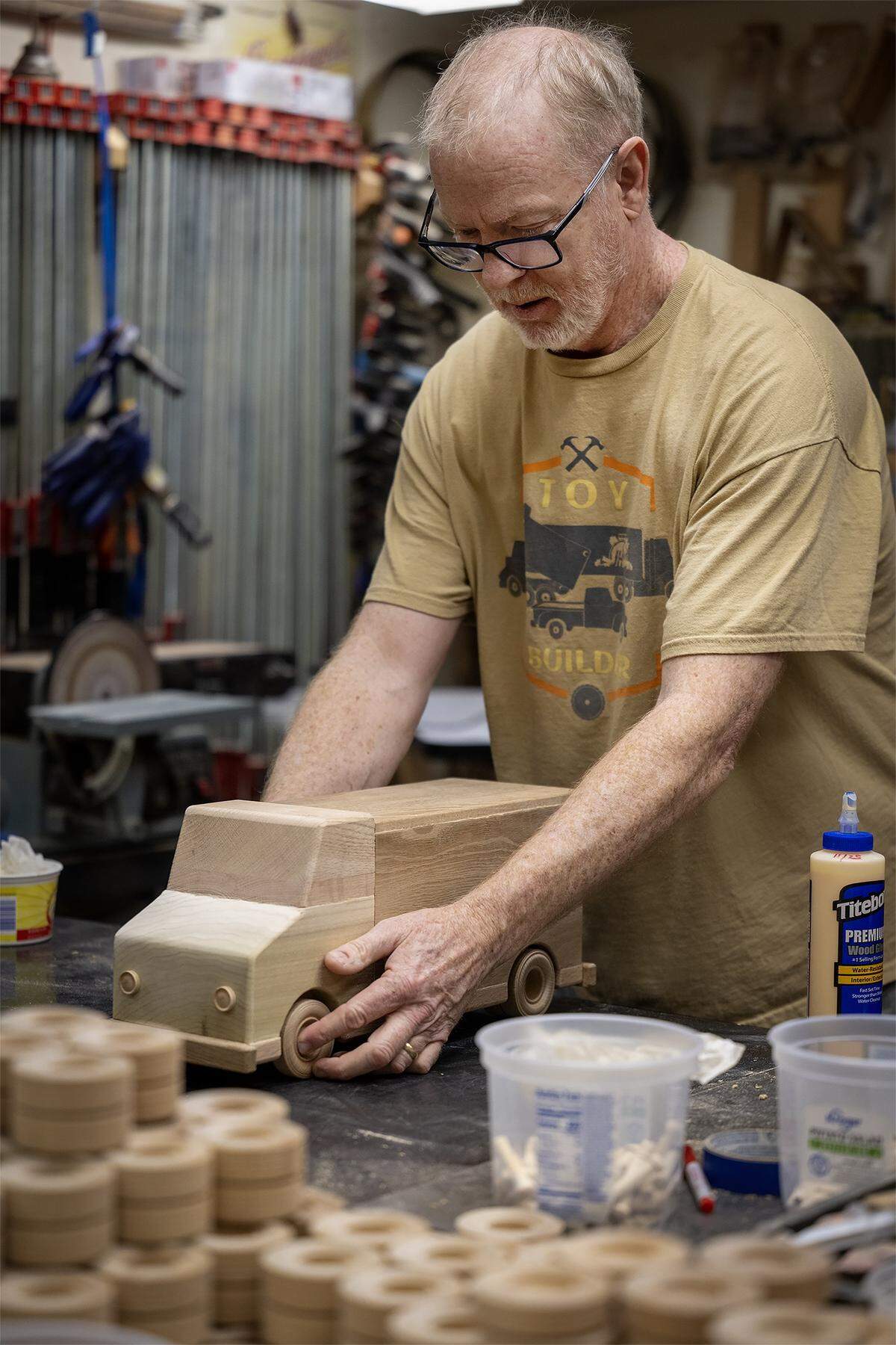 Jay Morris of JHM Woodworks carefully glues a wheel into place on a nearly-finished wood truck on Tuesday, Dec. 2, 2025, in Lawrence, Kansas. With donated wood scraps, Morris and a team of volunteers have handcrafted115 delivery-style trucks to be given to children in need through the Toys for Tots program.