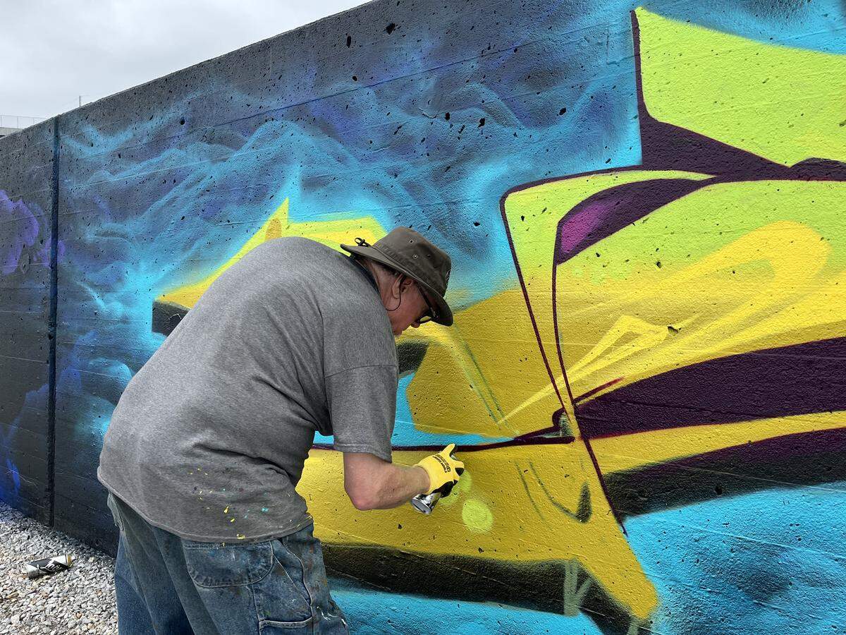 Gear, a local artists, spray paints his section of the MO River Mural on Friday May 22, 2026.