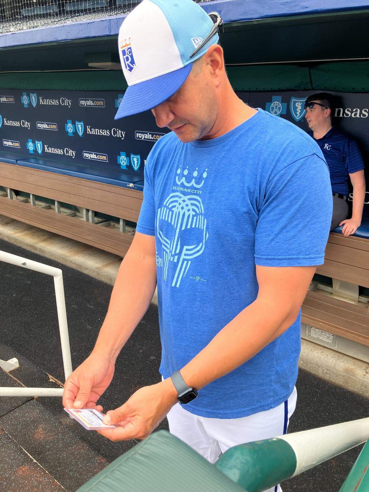 Royals pitching coach Brian Sweeney holds a baseball card of a 4-year-old named Charlie inside the Royals dugout.