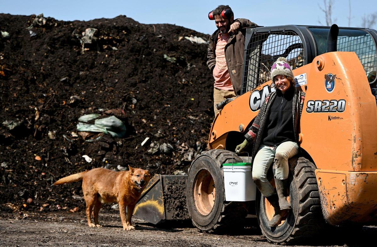 The composting operation of Compost Collective KC is run by Dan Heryer and Brooke Salvaggio of URBAVORE Farm, a Kansas City urban farm. Behind them and their dog Titan is a freshly turned compost heap. The goal of Compost Collective KC is to keep food waste out of landfills.