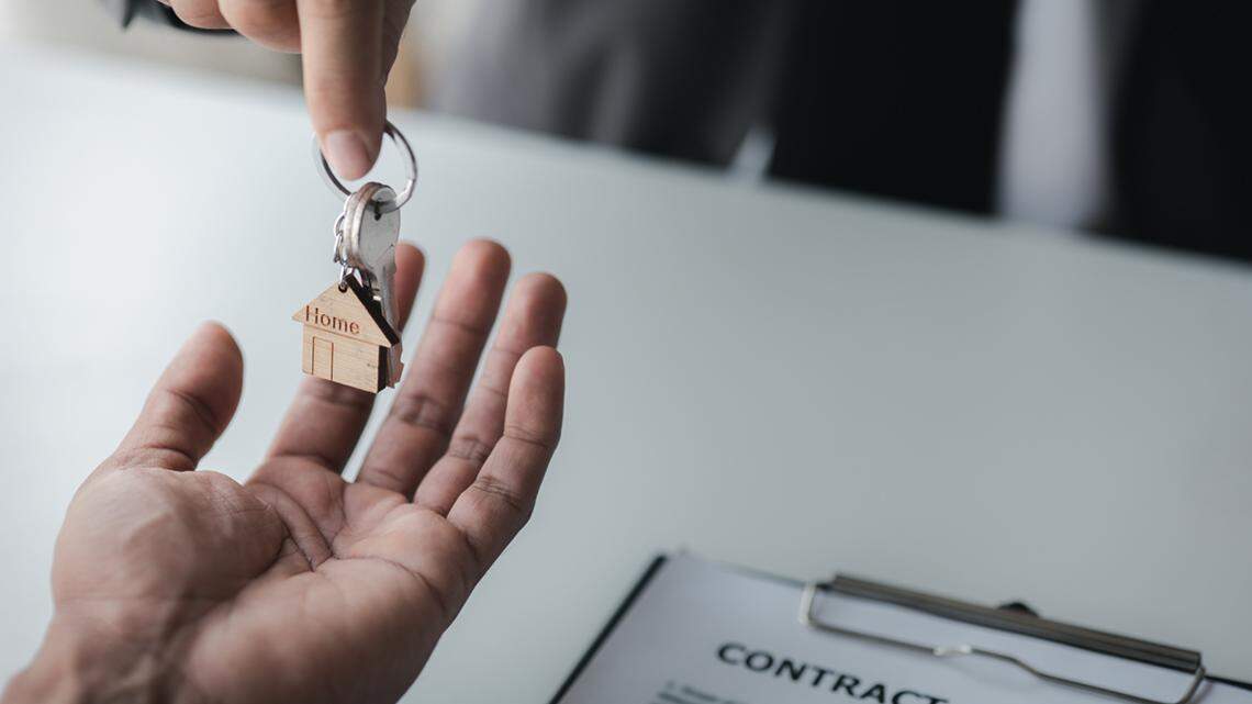 A home rental company employee is handing the house keys to a customer who has agreed to sign a rental contract, explaining the details and terms of the rental. Home and real estate rental ideas.