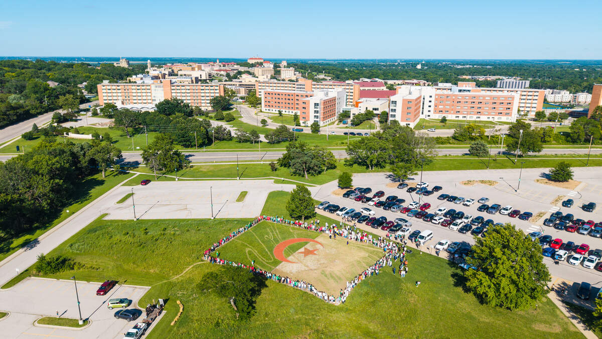 Earthwork artist Stan Herd spent five weeks constructing an earthwork art activation out of sand, grass, mulch and paving stones, revealed in an evening event on June 13, 2026. University of Kansas can be seen in the background, where volunteer coordinator that gathered the crowd Sajedah Andalsi goes to school. Herd praised her continued help with the project.