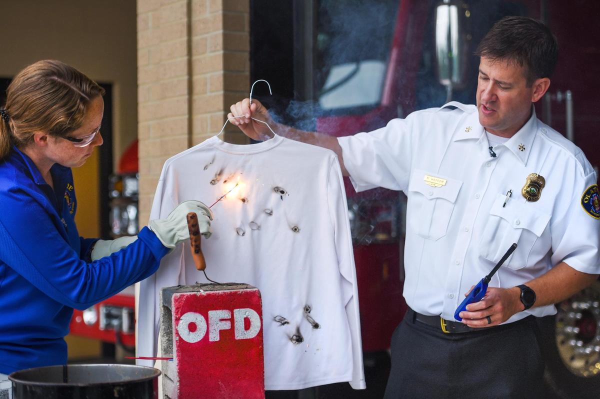 Michelle McLane, public education specialist for the Olathe Fire Department, and Olathe Assistant Fire Chief Mark Wassom demonstrate how easily a person could suffer burns when using sparklers. Synthetic fabrics burn more easily than natural fibers.