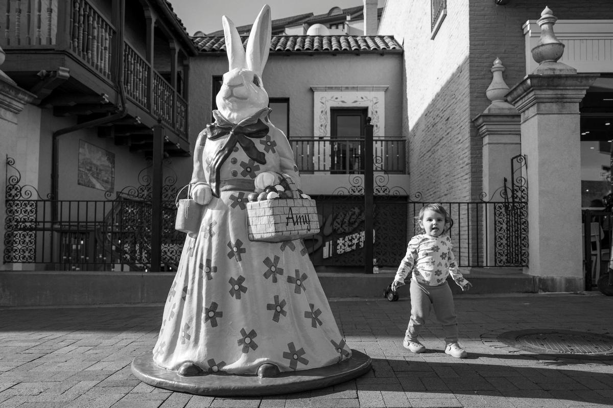 One-year-old Arielle Melendez plays beside Amy, an Easter bunny sculpture, along West 47th Street at the Country Club Plaza on Monday, April 14, 2025.