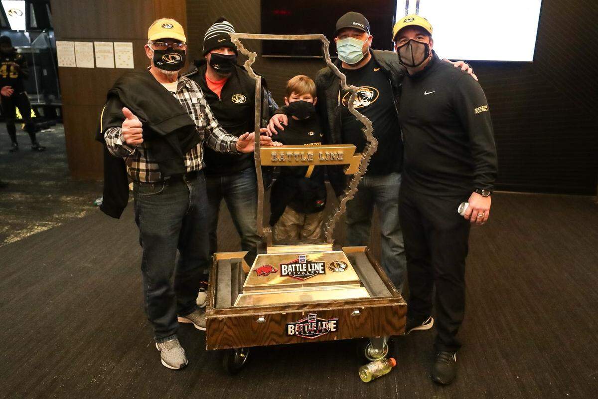 Three generations of Drinkwitz men gathered around the Missouri-Arkansas Battle Line Rivalry football trophy. From left: Jerry Drinkwitz, his son Zach, his grandson Jackson, his son Jeremy (Jackson’s father) and his son Eliah, the Mizzou football coach.