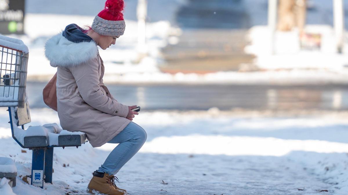 A commuter sits on a snow-covered bench while waiting for a bus following Kansas City’s first snowfall of the season on Sunday, Nov. 26, 2023.