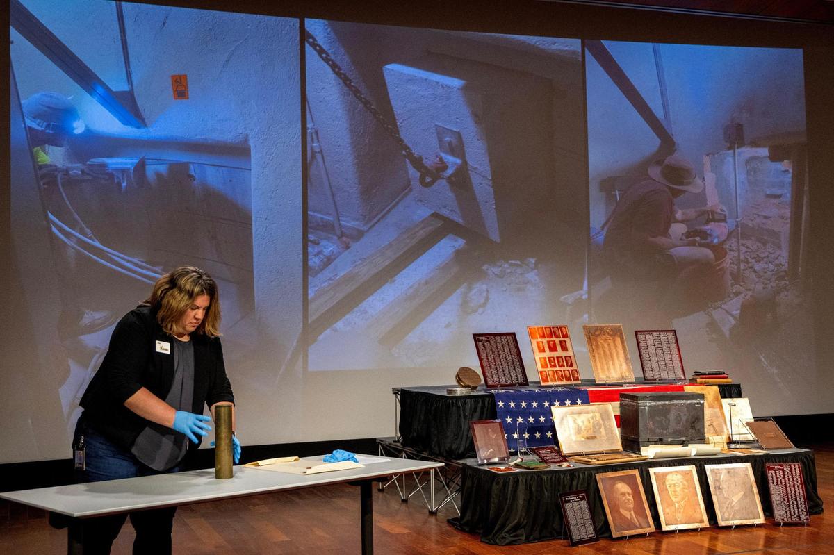 Stacie Peterson, director of exhibitions and collections at the National WWI Museum and Memorial, arranges artifacts on a table as photos of the 100-year-old time capsule’s recovery are displayed on a screen during an unveiling ceremony at the museum on Wednesday, Oct. 16, 2024, in Kansas City.