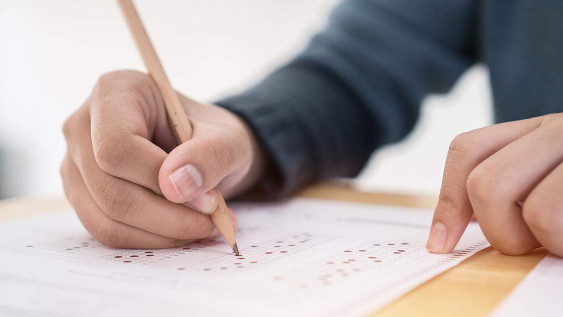 Education test exam concept, high school / university student holding pencil writing paper answer sheet on lecture chair for taking exams in examination room or classroom. Educational assessment ideas