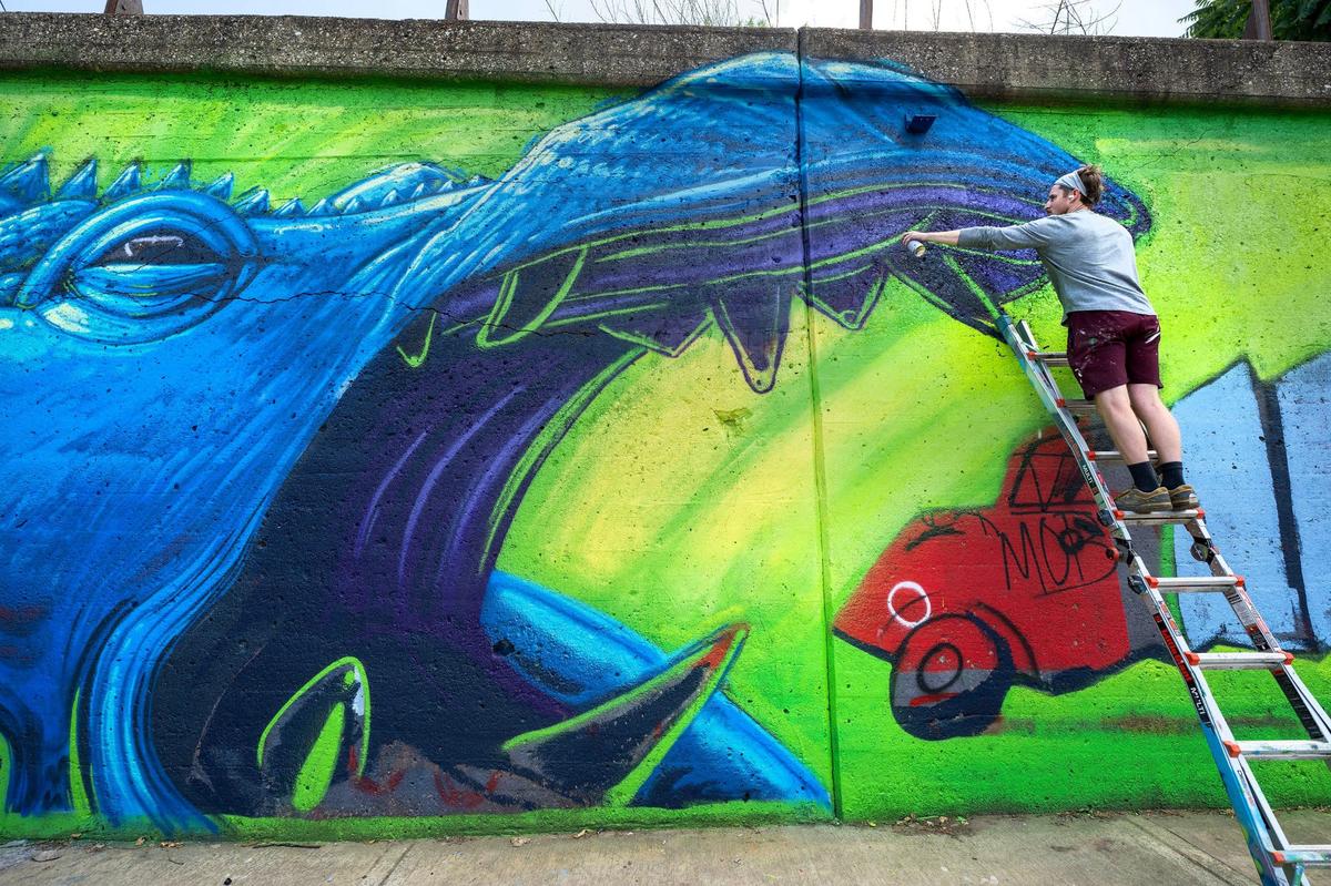 Working on his mural, Alex Eickhoff of Eye Cough Art, paints on the beast on the Independence Avenue truck-eating bridge in Kansas City.