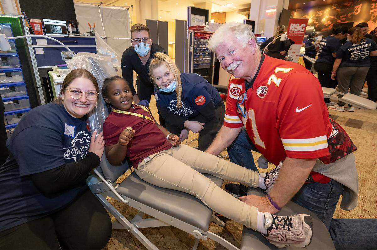 TeamSmile volunteers Rebecca Green, from left, Dr. Jordan Borzek, a dentist, and Linsey Titus, share a smile with Jaida Childs, 10,  of Kansas City and former Chiefs player Dave Lindstrom before Jaida receives free dental care during the TeamSmile Dental Tailgate at GEHA Field at Arrowhead Stadium on Tuesday, Sept. 9, 2025. Supported by the Kansas City Chiefs, over 200 volunteer dentists, hygienists, and dental assistants provided free dental services to 300 children from Kansas City, Missouri, and Kansas City, Kansas schools.