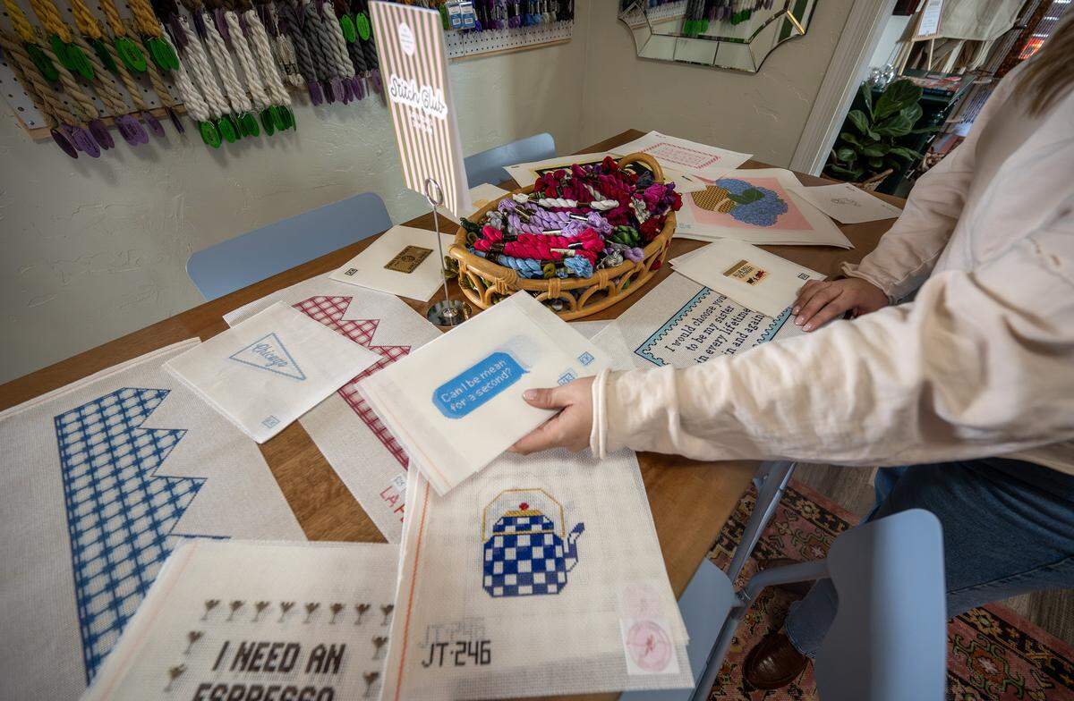 Sydney Kinkade, owner of The Parkville Needlepoint House, arranges needlepoint canvases on a table on Wednesday, Feb. 11, 2026, at the shop in Parkville.