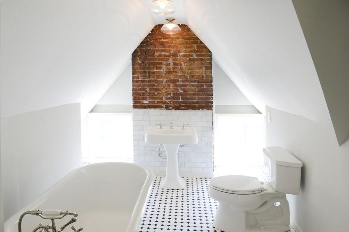 A brick wall punctuates an otherwise all-white guest bathroom with a pitched roof.