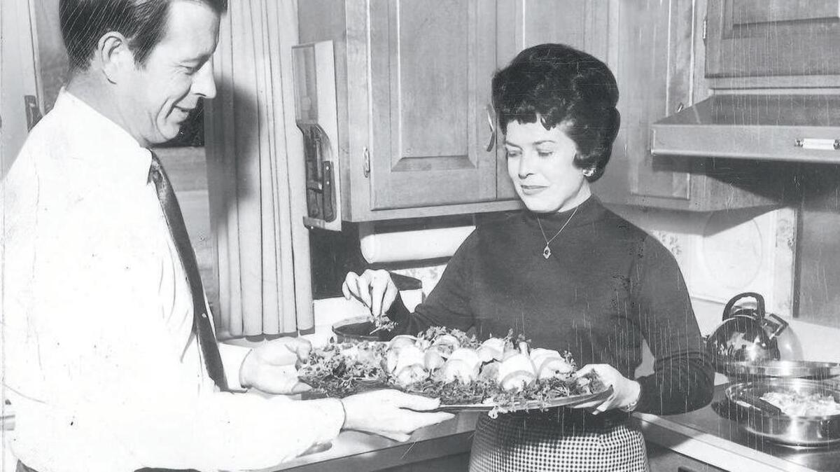 The Come Into My Kitchen column has featured recipes both simple and exotic in its 60 years. Here, Mrs. Charles Dorman hands her husband a platter of quail trimmed with bacon for an annual wild game dinner they hosted.