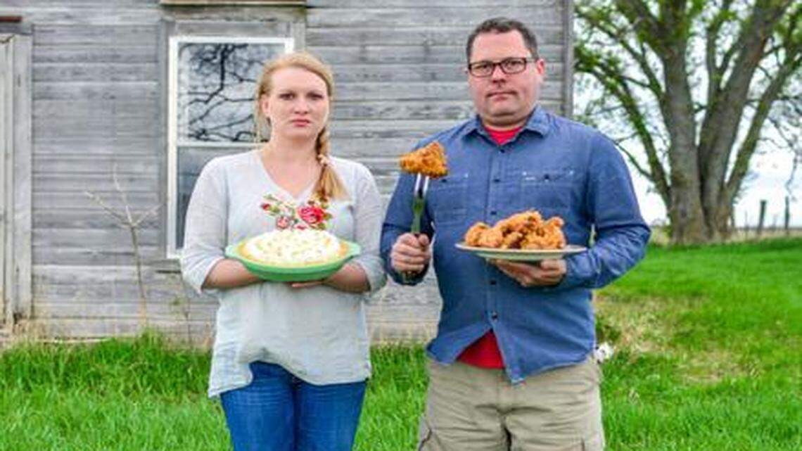 
American Gothic redux: Megan and Colby Garrelts stand in front of a weathered wood farmhouse in rural Parker, Kan. She holds a banana cream pie. Instead of a pitchfork, he has stuck a carving fork into a piece of Rye’s fried chicken. The photo appears in their new cookbook, “Made in America.”
