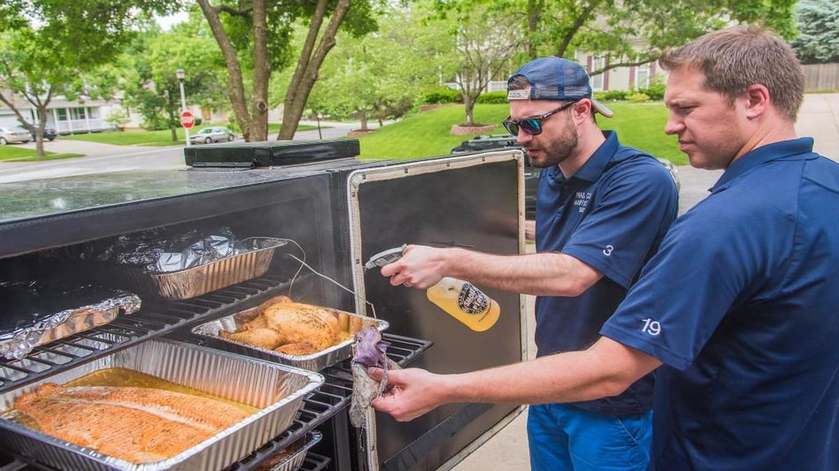 Garrett Schwede (foreground) and Matt Havens worked to keep the salmon and chicken moist. Schwede and Havens are two of the second generation of Mad Cow Angry Beaver, a competition barbecue team formed by a group of fathers as a way to spend time with their sons.