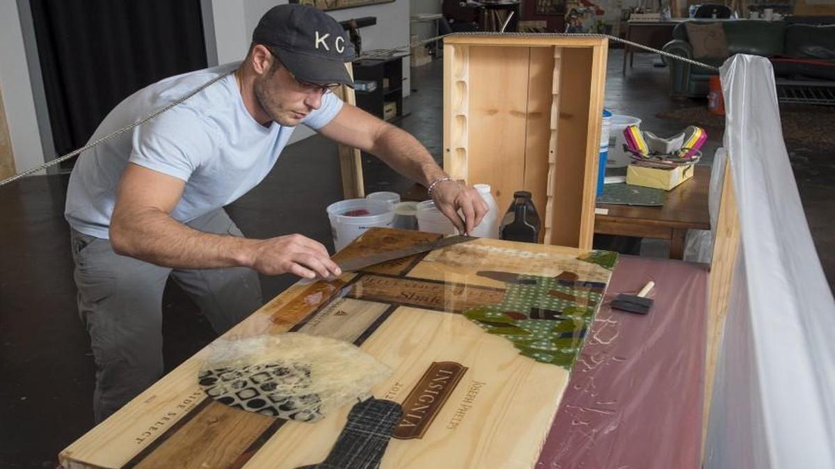 Travis Stewart carefully places a piece of metal from a whiskey barrel onto a piece of artwork he is creating in his Crossroads studio. When he is not tending bar, Stewart creates distinctive multi-dimensional pieces of art that reflect his love of bartending and craft cocktails.
